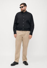 Black button-up shirt with long sleeves, tan chinos, and black shoes. The shirt features a small logo on the chest.