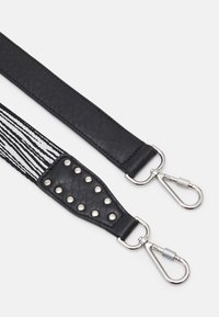 Deux sangles de sac noires avec mousquetons en métal argenté, une sangle en cuir noir uni et l'autre rayée noir et blanc avec des clous métalliques.