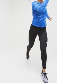 Sininen teksturoitu pitkähihainen urheilu paita yhdistettynä mustiin legginsseihin ja harmaisiin urheilukenkiin. Legginsseissä huomattava Nike-logo.