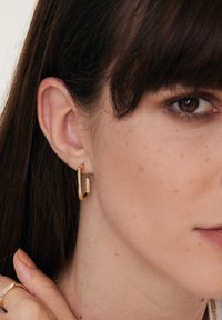 Złoty geometryczny kolczyk w kształcie obręczy o czystym, kanciastym designie. Polerowane wykończenie podkreśla elegancki kontur, dopełniając ucho noszącego.