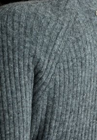 Pull gris à côtes avec un col haut, en matière douce, présentant des lignes texturées horizontales et un petit détail de bouton.