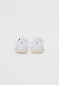 White sneakers with mesh fabric, a smooth rubber sole, flat laces, and a small logo tag on the heel. Simple design, rear view.