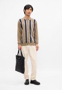 Brun och marinrandig kofta, krämfärgade byxor, svarta skor och en svart tölp. Koftan har knäppning och en mjuk textur.