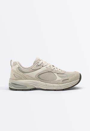 Beige athletic sneaker with mesh and suede panels, cushioned sole, lace-up design, and pull tab at heel, shown in side profile on white background.