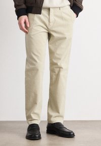 Calças de veludo cotelê bege com uma superfície texturizada, corte slim, e bolsos standard, combinadas com sapatos mocassim pretos num chão liso.