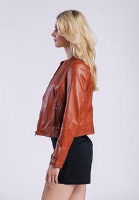 Bruine leren jas met een aansluitend ontwerp, een ronde halslijn, zijzakken en een gladde textuur. Draagt met een zwarte rok.