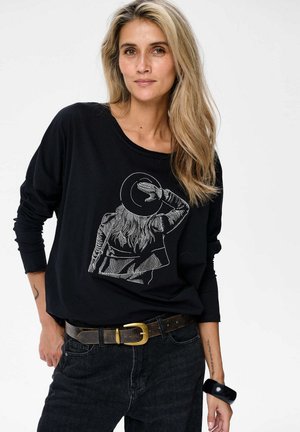 Zwarte longsleeve tshirt met een afbeelding van een persoon in een hoed, gecombineerd met donkere jeans en een bruine riem met een gouden gesp.