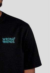 Černé bavlněné tričko s tyrkysovým logem "WRONG FRIENDS". Kružkový výstřih, krátké rukávy a hladká textura.