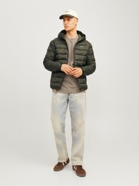 Dunkelgrüne Pufferjacke mit horizontaler Steppung, kombiniert mit einem grauen Rundhals-Shirt, hellblauen Jeans und braunen Sneakers.