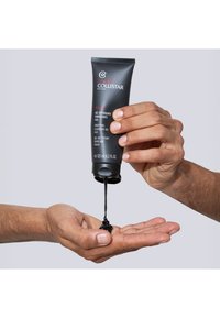 Czarny �żel oczyszczający jest wydobywany z matowej czarnej tubki. Dwie ręce są ustawione, jedna trzyma tubkę, a druga łapie żel.