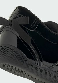 Gros plan sur le talon brillant d'une basket noire avec un nœud en satin noir et une semelle en caoutchouc texturée.