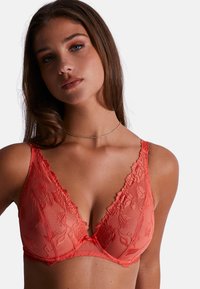Bralette en dentelle corail avec un décolleté en V profond, broderies florales et bordures décoratives sur les bretelles. Matière en mesh doux avec un aspect transparent.
