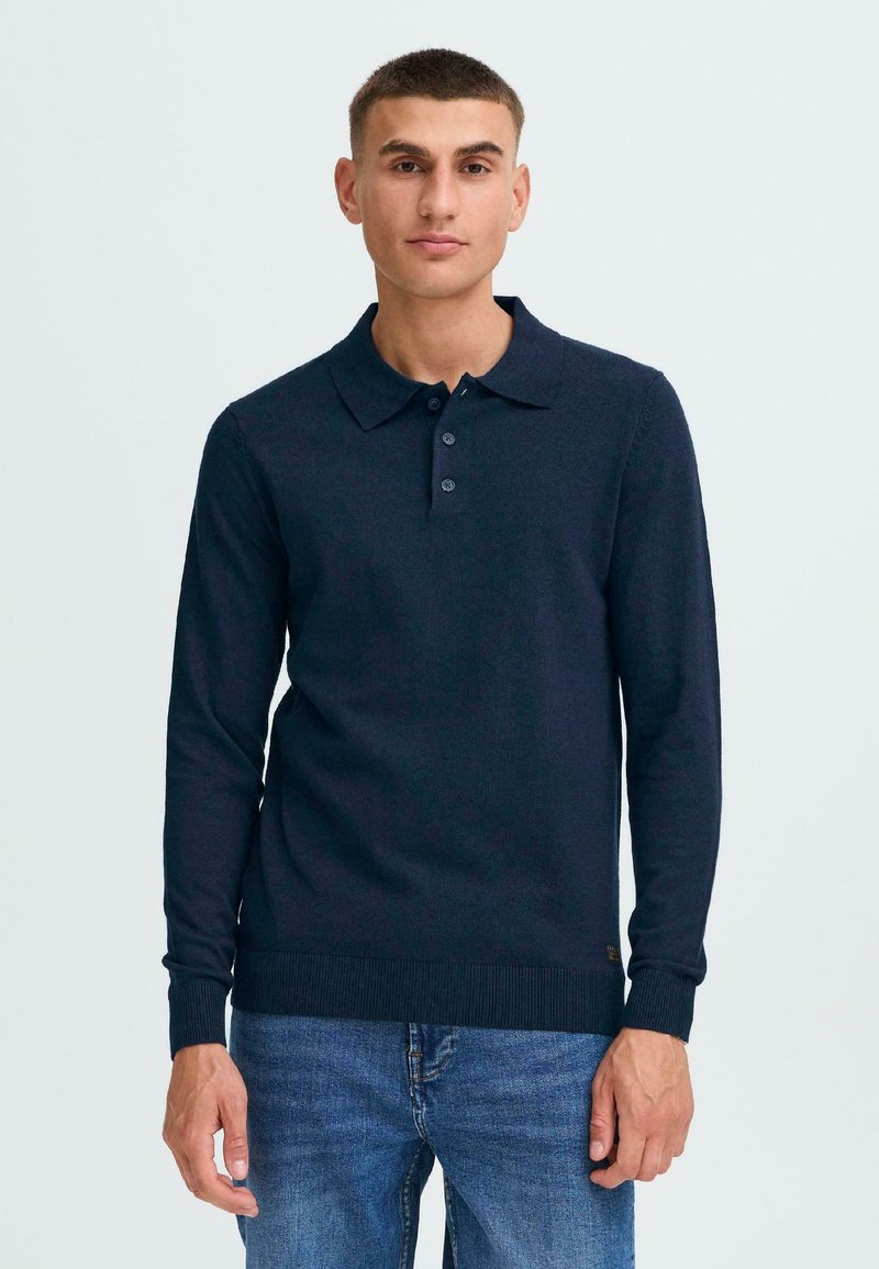 Marineblå langermet polo med ribbestrikket krage, tre-knappers plakk og teksturert stoff. Kombinert med blå jeans.