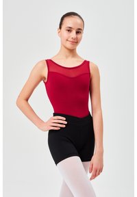 Roter ärmelloser Body mit transparentem Ausschnitt und schwarzen hochgeschnittenen Shorts. Das Model trägt weiße Strumpfhosen und posiert mit einer Hand auf der Hüfte.