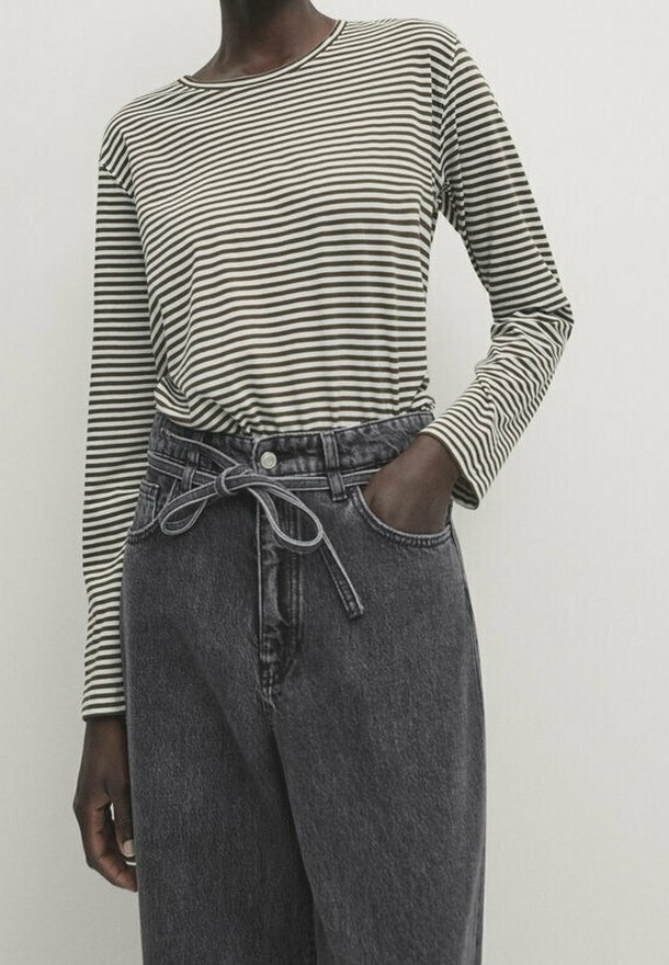 Gestreiftes langärmliges Hemd in Creme und Dunkelgrün, kombiniert mit hoch taillierten grauen Denim-Hosen mit Taillenzug und Knopfverschluss vorne.