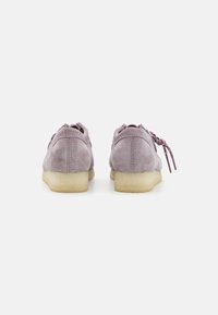 Zapatos de ante lilas con una textura suave, punta redonda y suelas de goma blanda; presentan cordones contrastantes y un diseño minimalista.
