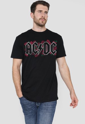 Black cotton t-shirt featuring "AC/DC" logo in gray with red roses. Short sleeves and a crew neckline, paired with blue jeans.