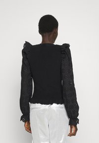 Schwarzes gestricktes Oberteil mit Rüschendetails und Broderie-Anglaise-Ärmeln. Verfügt über einen gewellten Saum und detaillierte florale Ausschnitte.