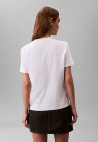 Fehér pamut rövid ujjú póló, kerek nyakkivágással és laza szabással, fekete rövid szoknyával párosítva, amely hátsó zsebekkel rendelkezik.