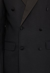 Svart dubbelknäppt kavaj med satinkrage, texturerad tyg, sex knappar och en enkel bröstficka.