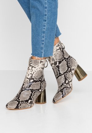 Enkellaarsjes met slangenprint en blokhakken van metaal, gedragen met cropped blauwe jeans op een witte vloer.