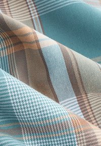 Tekstil i et ternet mønster med nuancer af teal, brun og creme. Struktureret stof med vævede detaljer og varierende stribebredder.