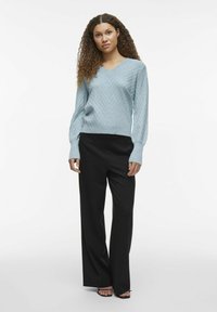 Lyseblå V-hals genser med en teksturert fiskebensmønster, kombinert med høyhårede, svarte, vide bukser.