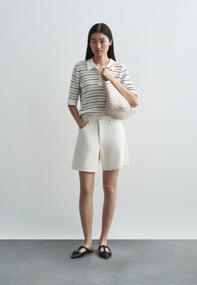 Vita bomullsshorts kombinerat med en randig stickad polotröja. En vävd väska i en ljus färg och svarta platta skor fulländar looken.