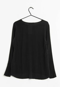 Haut noir à manches longues avec un col rond, fabriqué en tissu lisse, doté de fentes latérales et d'un ourlet droit, suspendu à un crochet noir.