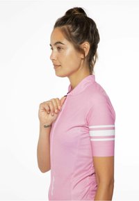 Ružová cyklistická dres s vysokým golierom, krátkymi rukávmi a bielymi pruhmi na rukávoch. Obsahuje zips a detail loga na boku.