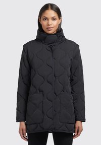 Doudoune noire matelassée avec un col haut, fermeture �à pression et deux poches avant ; présente un motif de couture ondulé pour la texture.