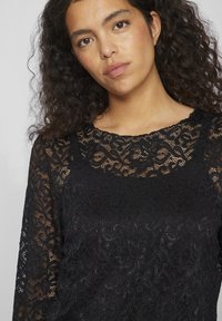 Black lace top featuring a floral pattern, long sleeves, and a round neckline. The fabric is semi-sheer with intricate detailing throughout.