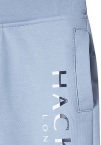 I pantaloni da tuta azzurri chiari presentano una morbida texture di tessuto, una tasca laterale e una stampa audace in bianco e nero con la scritta "HACK."