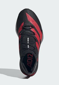 Black and red athletic shoe with a textured upper, featuring angular black stripes, lace closure, and a cushioned sole.