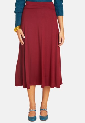 Woman wearing a burgundy midi skirt, teal long-sleeve top, gold bangles, and teal Mary Jane shoes with buckle straps.