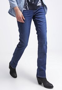 Modré džínov�é kalhoty s rovným střihem, středně těžká látka a jemná textura. Kombinovány s černými kotníkovými botami na podpatku a lehkou bundou.