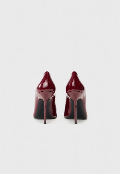 Pantofi cu toc din piele patent în nuanța burgundă, cu vârf ascuțit și toc subțire stiletto. Finisaj neted și talpă neagră.