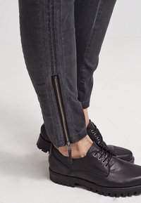Zwarte slim-fit broek met een ritssluiting bij de enkel en getextureerde zijstrepen, gecombineerd met zwarte leren schoenen met een getextureerde zool.