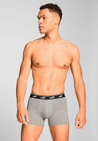 Gray boxer shorts with a black elastic waistband featuring the Puma logo. The fabric appears smooth and fitted. Model stands sideways.