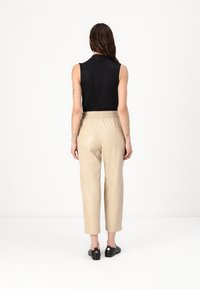 Zwarte mouwloze top met hoge kraag, gecombineerd met lichtbeige leren broeken met een elastische tailleband en tapering pijpen.