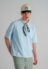 Light blue cotton t-shirt with short sleeves, paired with a cream and green cap, and a patterned scarf tied around the neck.