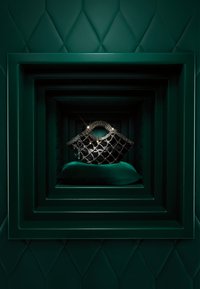 Schwarze gesteppte Handtasche mit metallischen Akzenten, präsentiert auf einem grünen Samtkissen, umrahmt von geschichteten grünen geometrischen Hintergründen.