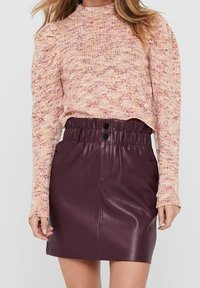 Pull en tricot dans des tons doux de rose et de crème avec un col haut, associé à une jupe moulante en simili cuir bordeaux dotée d'une taille élastique et de deux boutons.