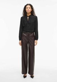 Blouse noire texturée avec un décolleté en goutte, associée à un pantalon large en cuir bordeaux taille haute et des talons noirs.