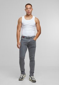 Jeans ajustados grises con una etiqueta de acento roja, combinados con una camiseta sin mangas blanca y zapatillas en blanco y negro. Tejido suave, corte slim.