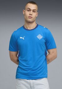 Αθλητική φανέλα Puma blue με κοντά μανίκια, στρογγυλή λαιμόκοψη, λευκές λογότυπικές λεπτομέρειες και πλέγμα πλαϊνές πάνελ. Ομαλή υφή υφάσματος.