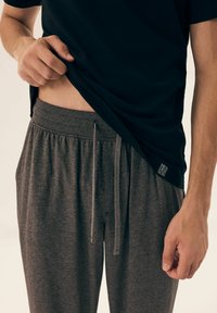 Grey joggers made of soft fabric with an elastic waistband and drawstring. A black shirt partially covers the waistband.