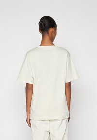 Cremefarvet oversized t-shirt med korte ærmer, rund halsudskæring og en afslappet pasform, lavet af blødt bomuldsstof. Minimalistisk design.