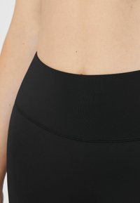 Leggings negros de talle alto hechos de una tela suave y elástica, con una cinturilla ancha y costuras sutiles para un aspecto elegante.