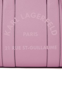 Lila textúrázott bőrfelület függőleges varrásokkal és domború felirattal: "Karl Lagerfeld Paris 21 Rue St-Guillaume."